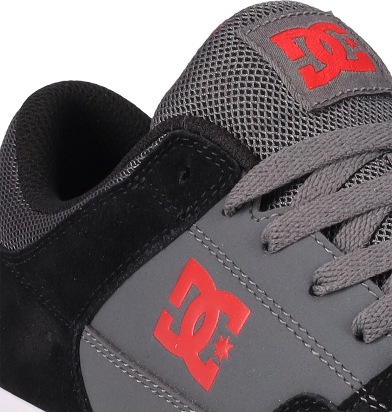 Close-up of DC Shoes Men's Onyx Shoes, showcasing a minimal vulc silhouette in black suede, gray leather and mesh, gray laces, with a red DC logo on the side and tongue. Only part of the shoe is visible.