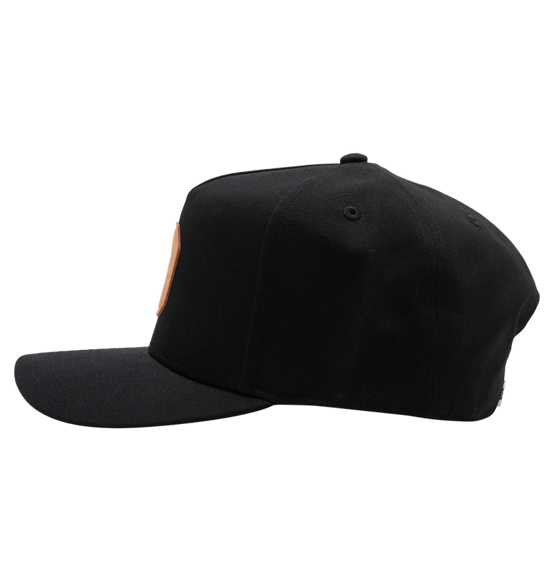 The Men's Reynotts Cap by DC Shoes is shown from the side against a white background, featuring a flat brim and a small round patch with subtle DC branding on the front.