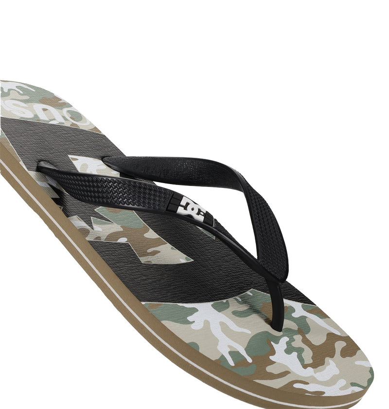 The image shows a Men's Spray Graffik Slide by DC Shoes, featuring a black strap with the DC logo and a green, beige, and white camouflage-patterned sole—ideal for post-skate comfort.