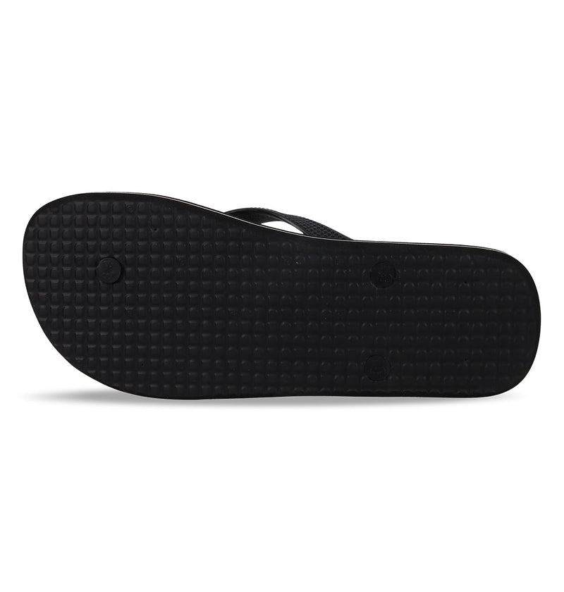 The image shows the bottom view of the Men's Spray Graffik Slides by DC Shoes, featuring a black slip-on design with a textured sole pattern and visible circular grip points.