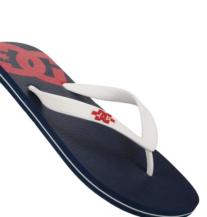 The Men's Spray Slides by DC Shoes are navy blue slip-on flip-flops with white straps and a bold red DC Shoes logo on both the straps and footbed, standing out sharply against a white background.