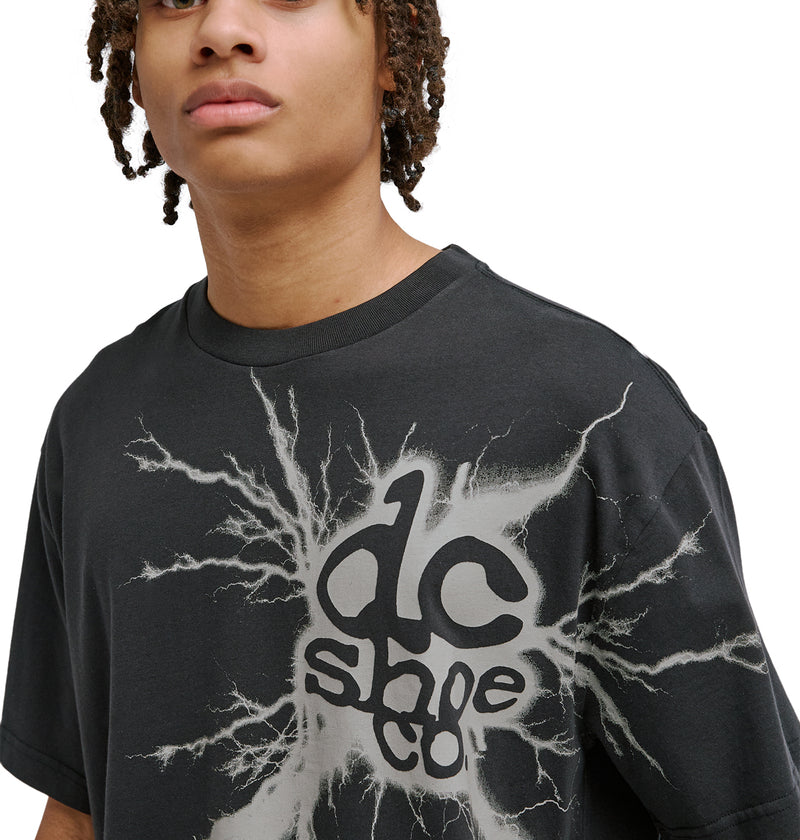 A person with medium skin and curly hair wears a black Reebok Strike Twice Hss t-shirt with a white lightning graphic and bold text on the front. Only the upper body and part of the face are visible.