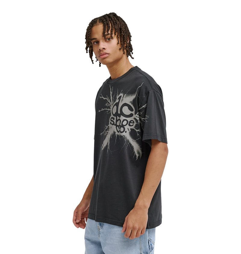 A young person with braided hair wears a black Reebok Strike Twice Hss t-shirt with a cracked graphic design and light blue jeans, posing against a plain white background.