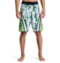 A person is seen barefoot, wearing Reebok Sylem 21 white board shorts featuring green and black abstract flame designs. The image is cropped at the waist and below the knees.