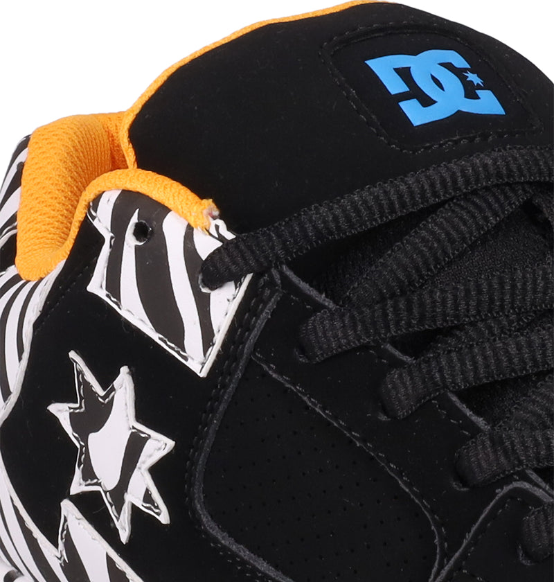 Close-up of Women's DC Command Shoes by DC Shoes—black skate shoes featuring white zebra-patterned stars, yellow lining, black laces, and a blue DC logo on the tongue that highlights their street-inspired style and authentic skate heritage.
